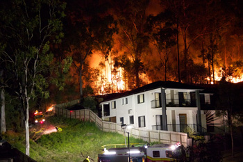 Bushfire burning close behind a large house at night.
