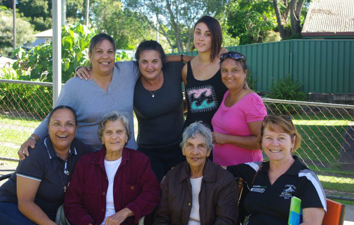 Eight smiling women facing the camera with arms around each other