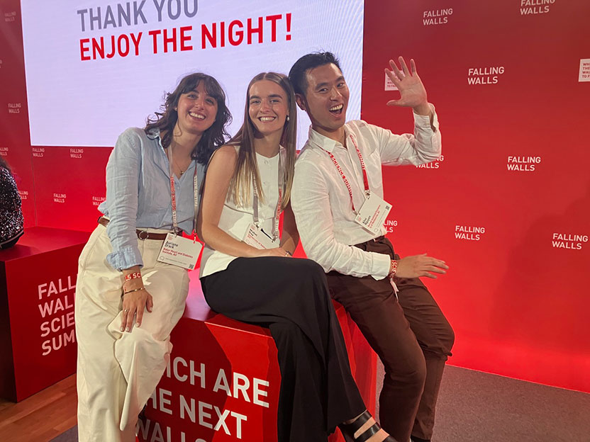 Three people sitting on red benches at the Falling Walls Science Summit with a sign reading 'Enjoy the Night!'