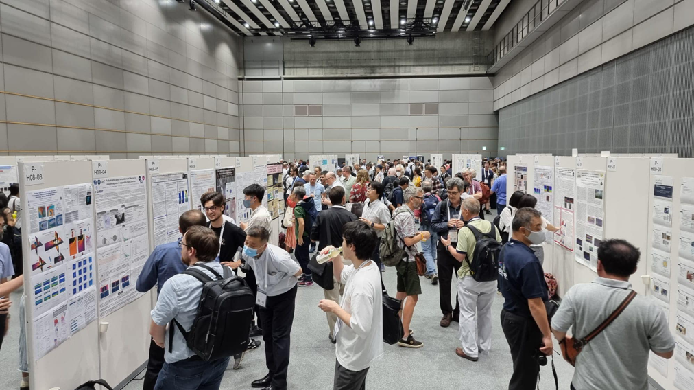 A room filled with a crowd of people looking at scientific posters affixed to three walls of the room.