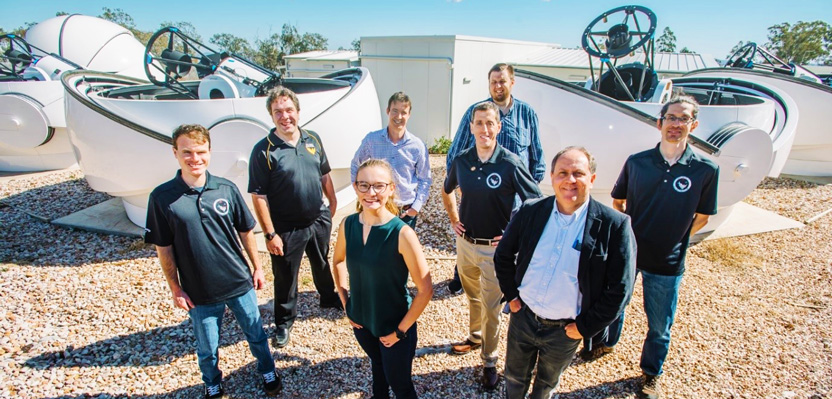 Group of smiling people, one woman and seven  men, in front of several rounded structures that hold telescopes