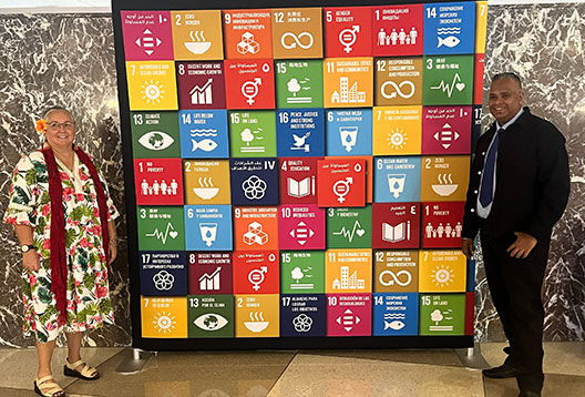 Dr Christina Newport and Dr Awnesh Singh at the United Nations standing next to a colourful board of the Sustainable Development Goal tiles