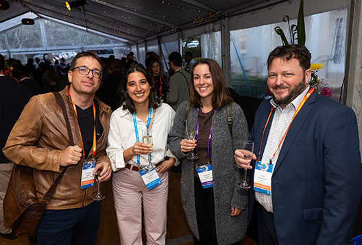 Four people smiling, wearing conference lanyards and holding drinks