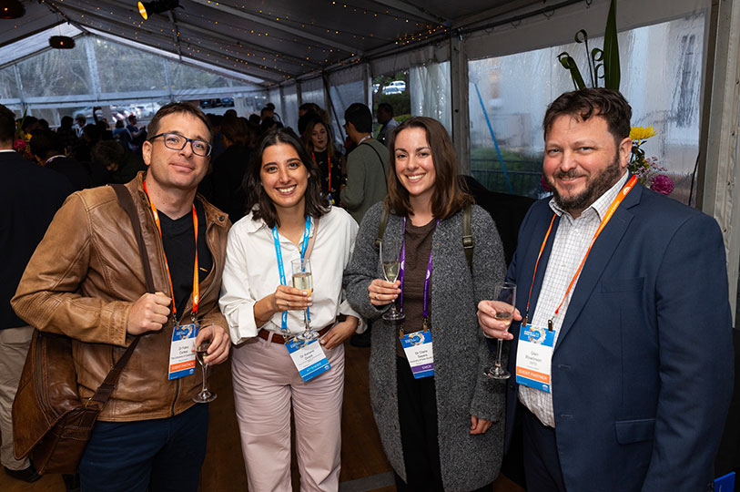 Four people smiling and wearing conference lanyards at a networking event