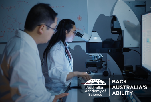 Two scientists at a microscope in a dimly lit lab with the overlaid text 'Back Australia's ability'