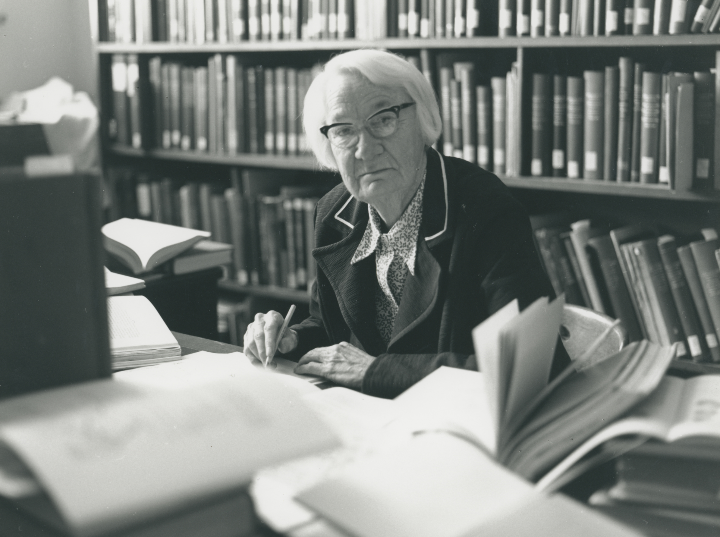 Dorothy Hill working at a desk with bookshelves behind