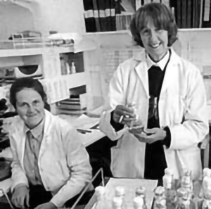 Two female scientists in white lab coats, smiling and looking relaxed (black and white photo)
