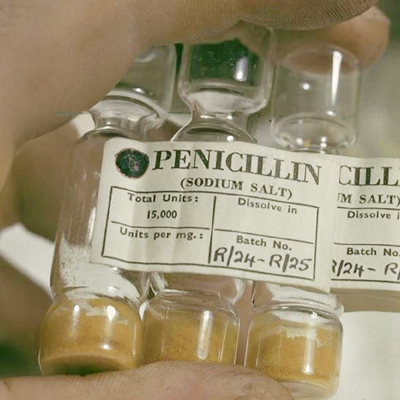 Fingers holding three small glass vials with yellowish material in the bottom of each vial, labelled 'PENICILLIN (SODIUM SALT) Total Units: 15,000; Batch No. R/24-R/25'