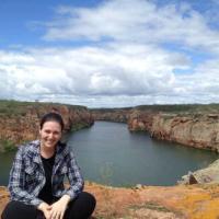 Dr Camilla Di Nizo, crouched in front of a canyon with water.